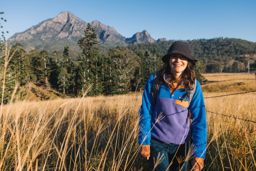 Bec stands in a field with Mt Barney in the background